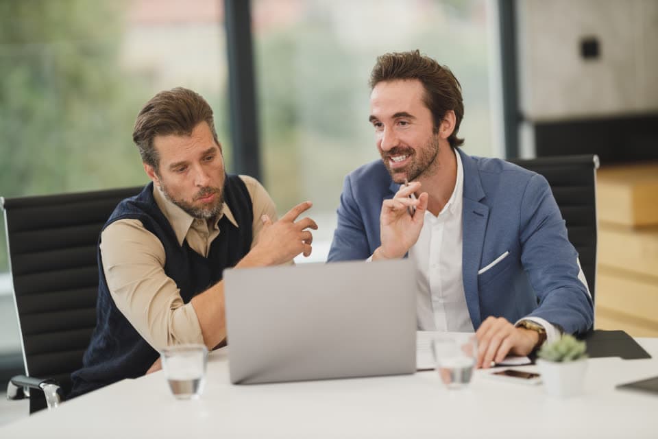 Two people look at a laptop together in a meeting room